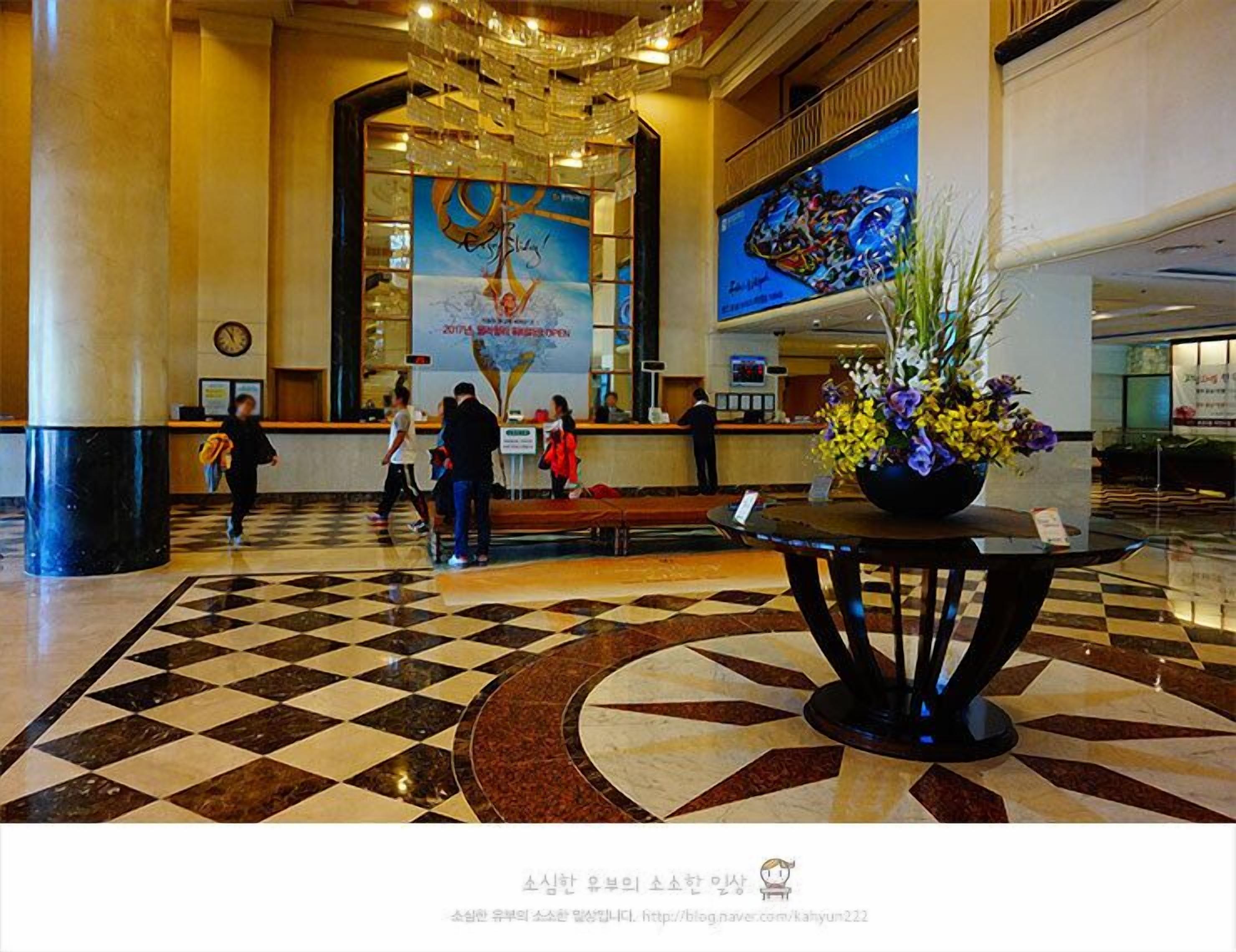 A lobby with a check-in counter, a large poster, and a decorative plant.