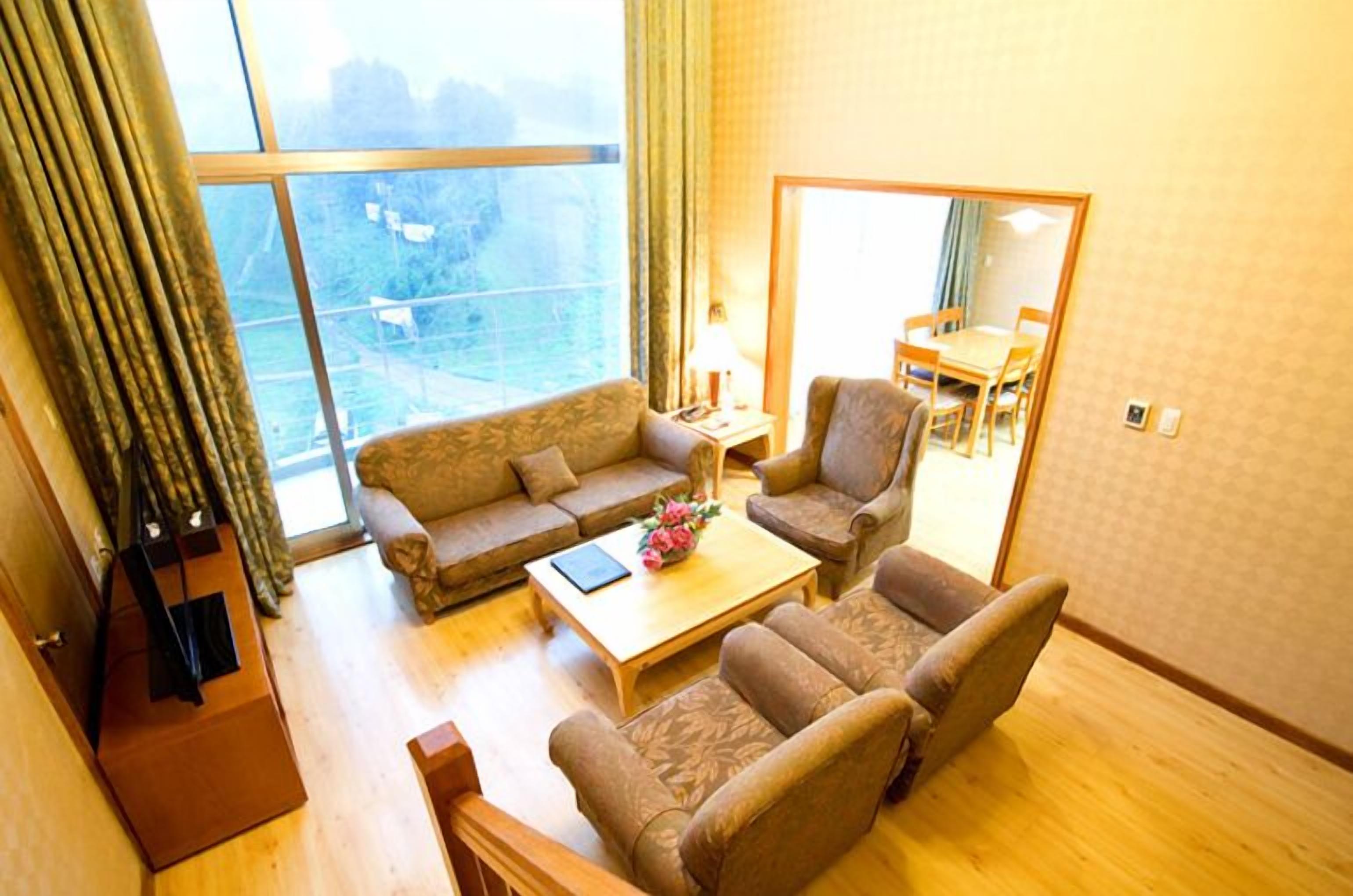 A living room with a sofa, armchair, and coffee table, a dining table with chairs, and a large window with curtains.