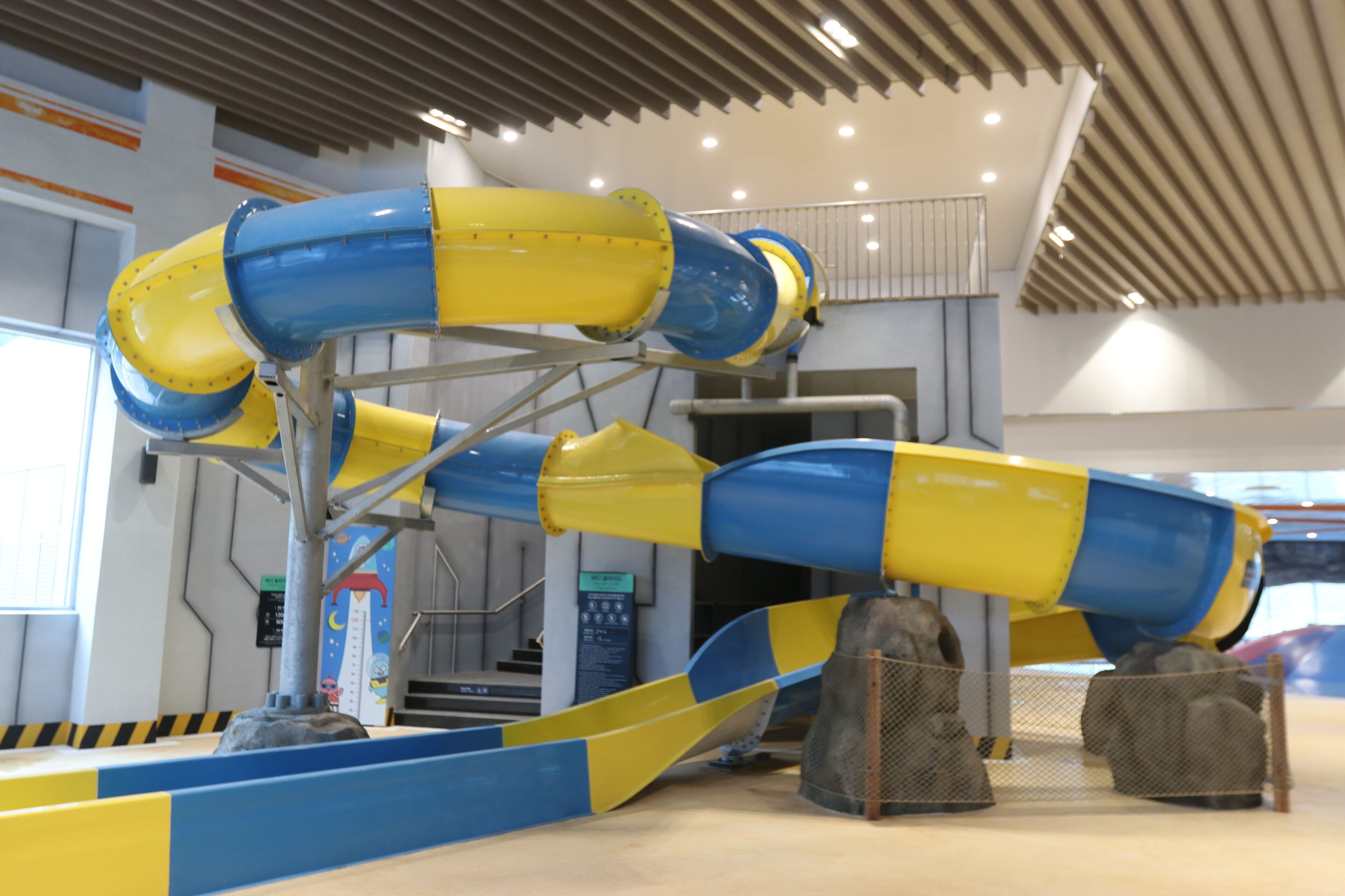 A water slide structure with yellow and blue tubes, metal supports, and safety barriers.