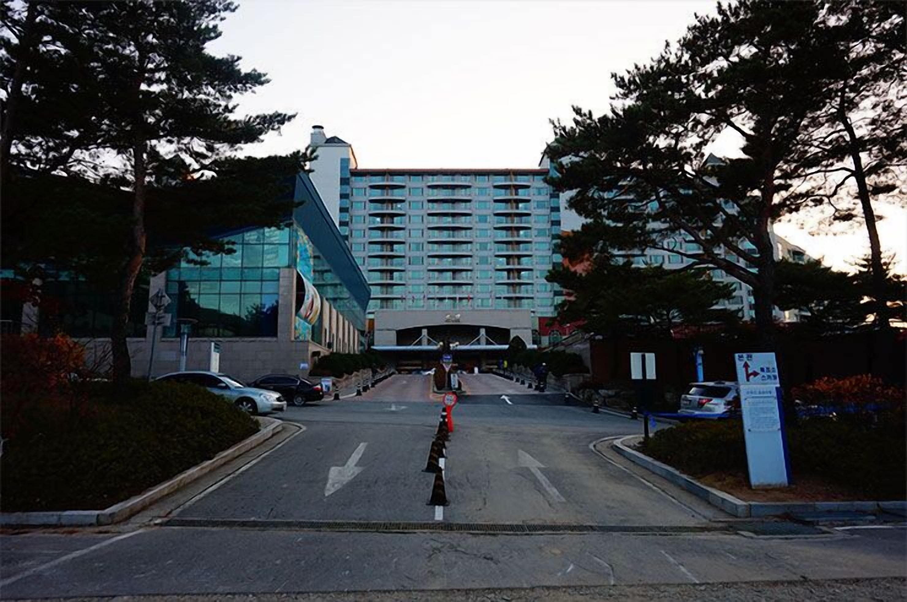A hotel entrance with a modern building, a parking area, and a clear sky.