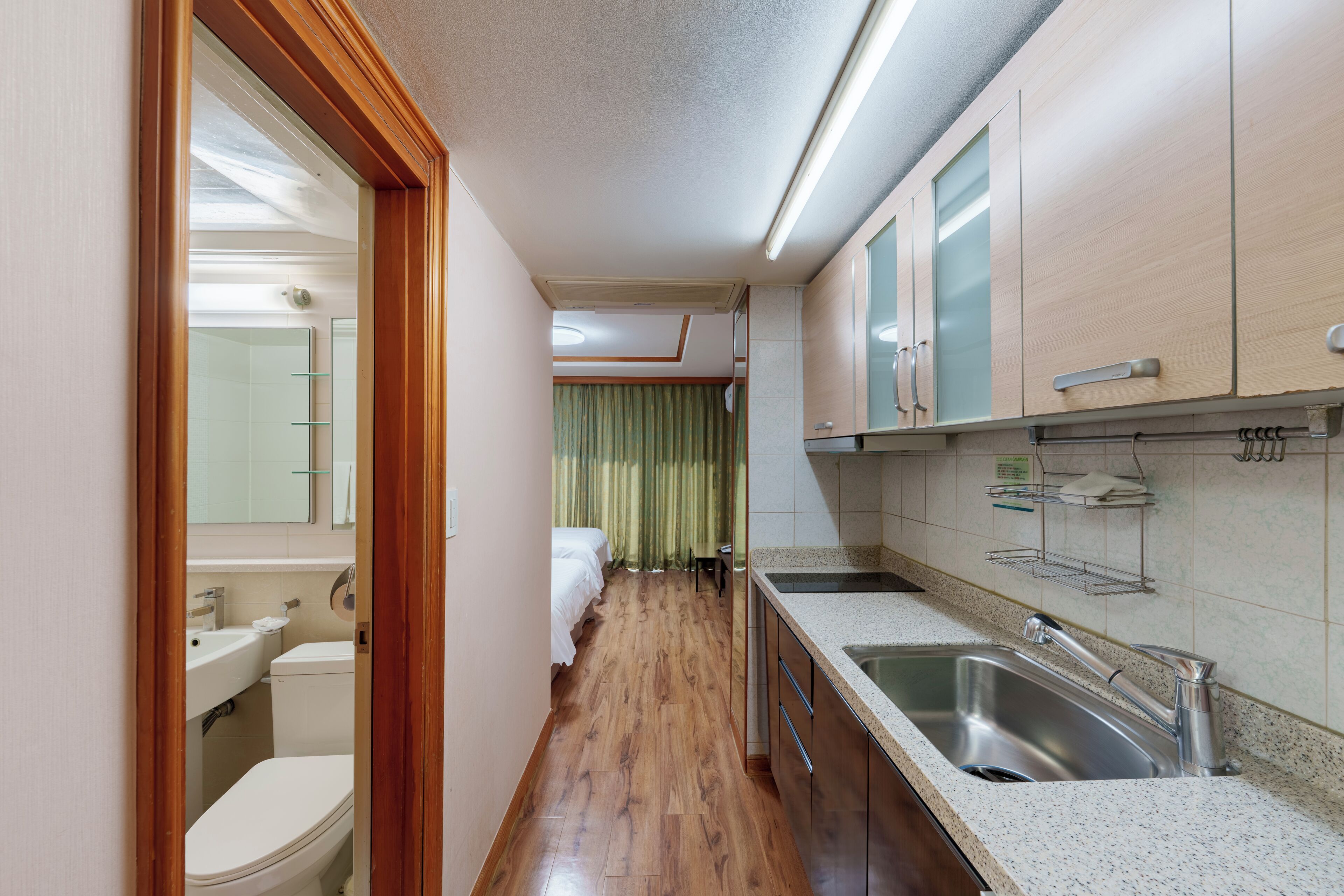 A narrow hallway leading to a bathroom and a kitchenette with a sink and cabinets.