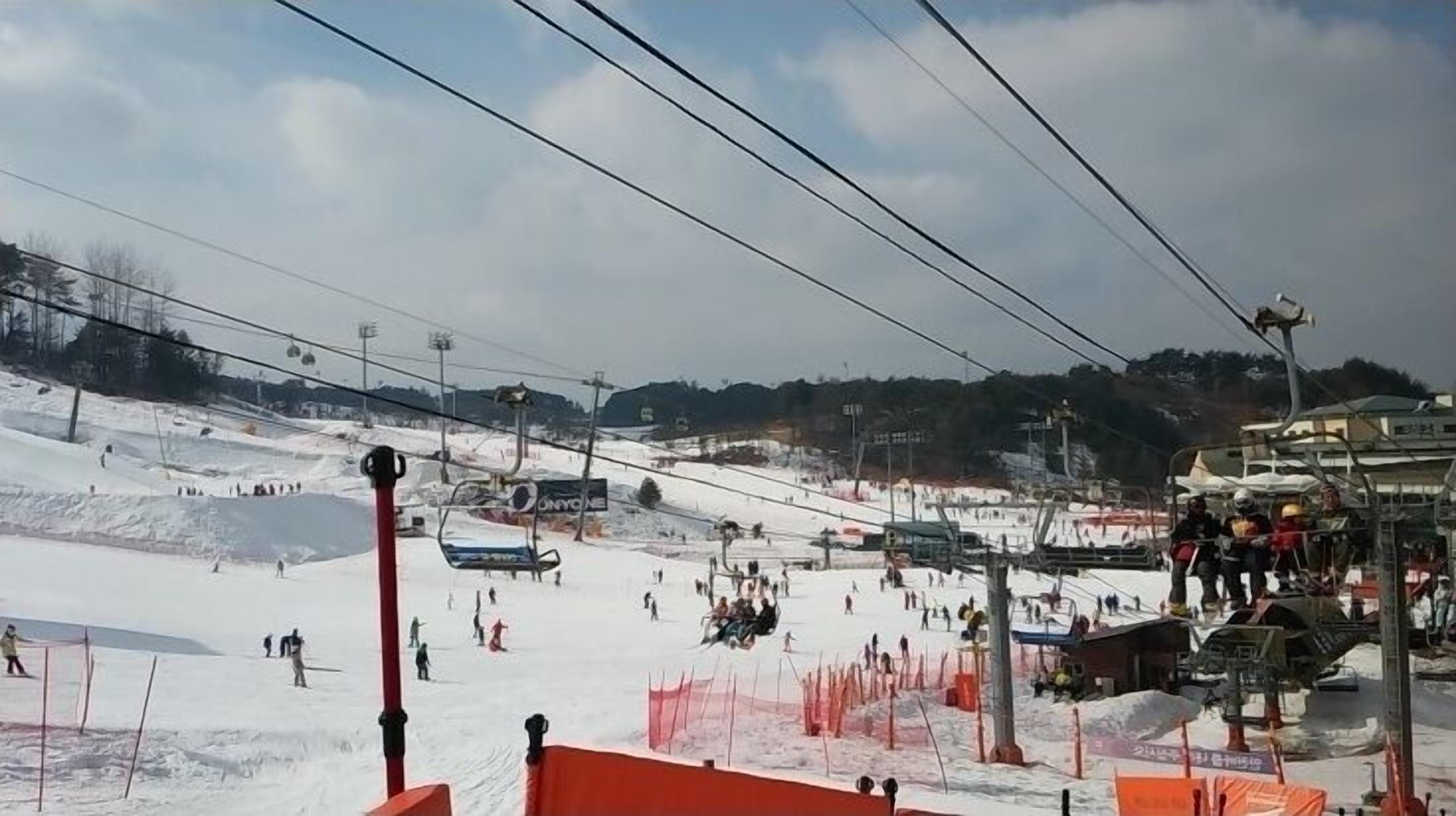 A ski slope with a chairlift, skiers, and a ski lodge in the background.