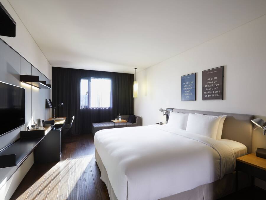 Una habitación de hotel moderna con una cama grande, un televisor de pantalla plana, un escritorio y un área de estar cómoda.