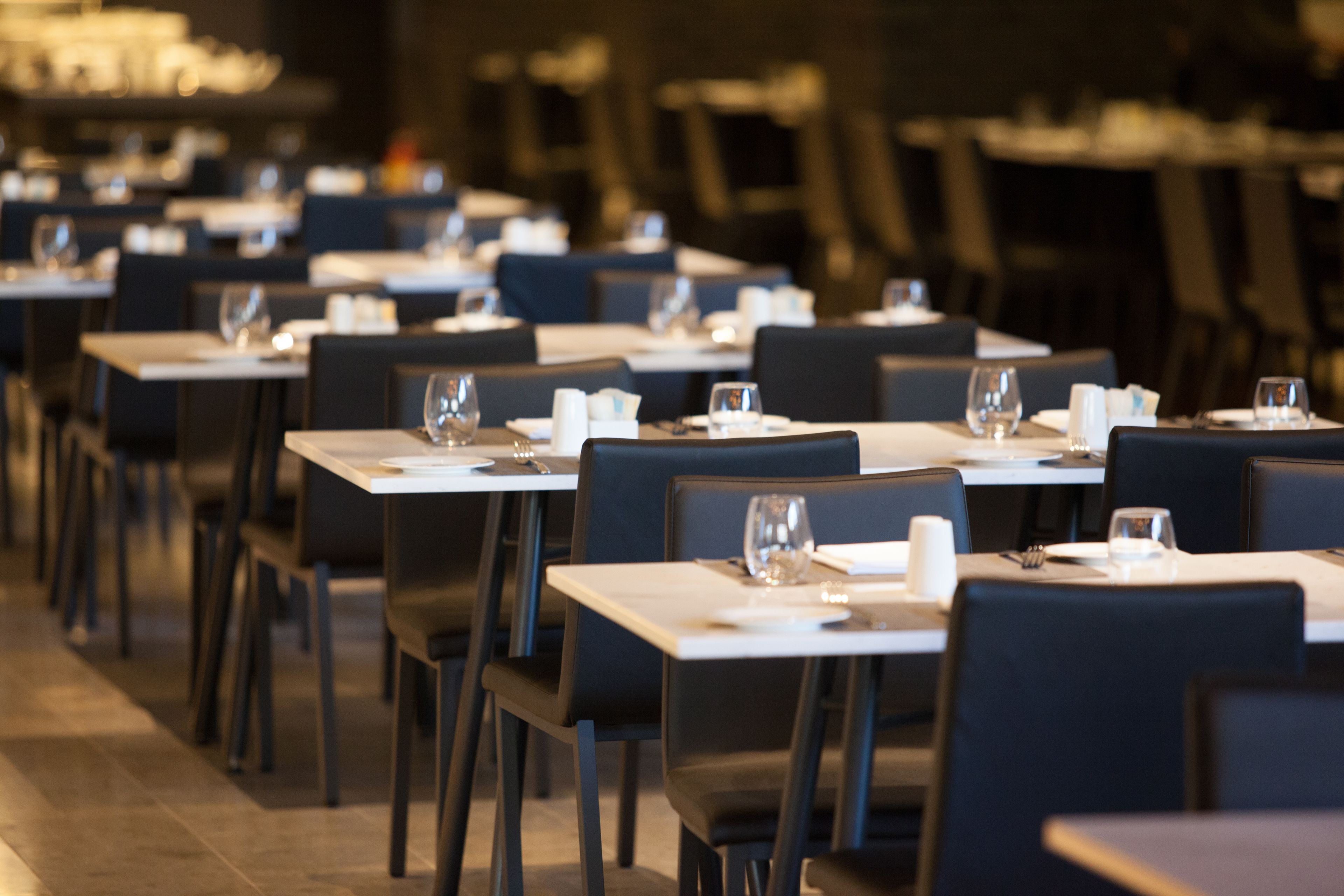 Un restaurante con varias mesas y sillas, cada conjunto con mantel blanco, platos y cubiertos.