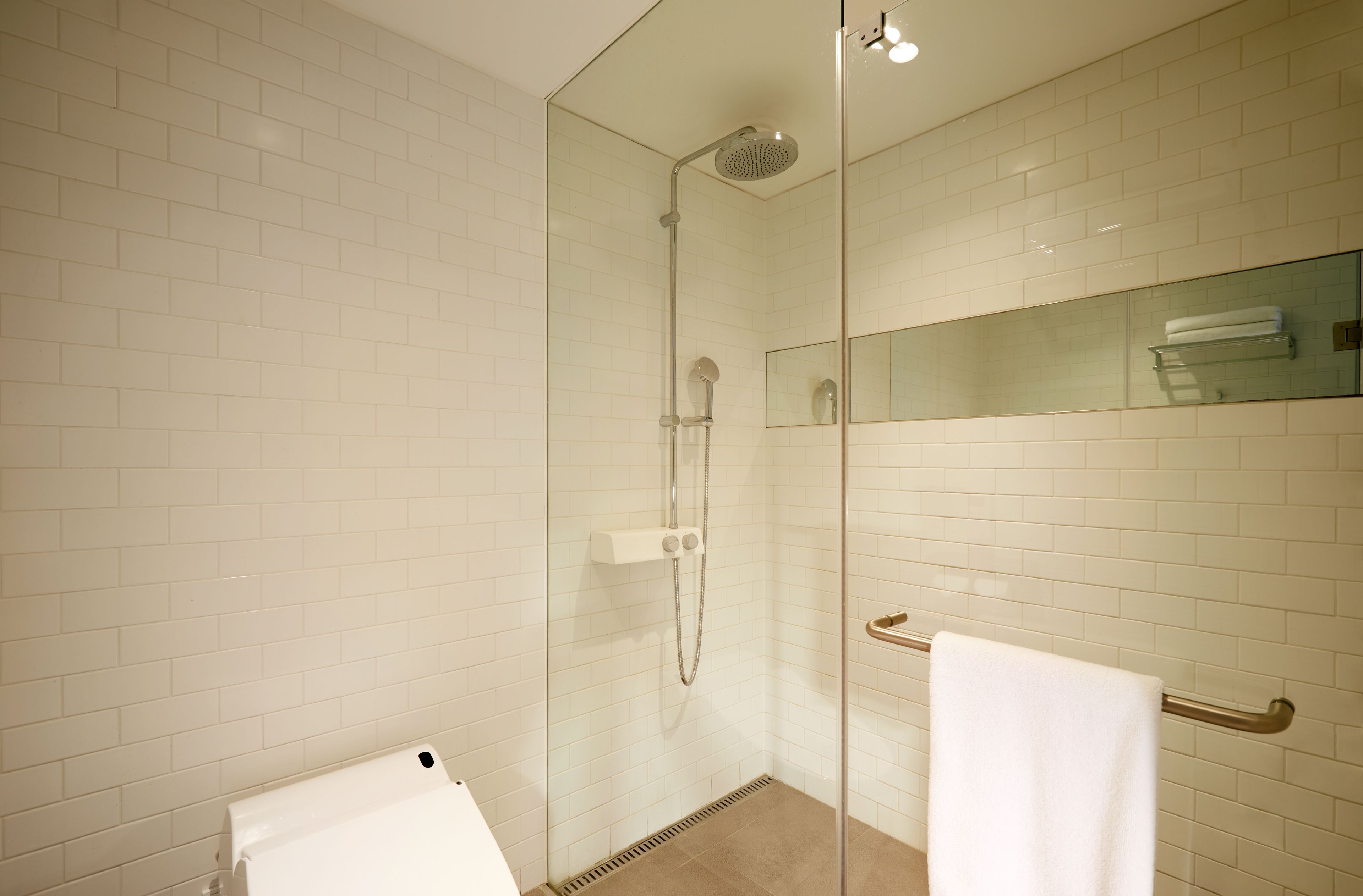 Un baño moderno con azulejos blancos tipo metro, una ducha con mampara de vidrio, un estante de vidrio con una toalla y una toalla blanca colgada en un perchero.