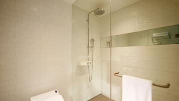 Un baño moderno con azulejos blancos tipo metro, una ducha con mampara de vidrio, un estante de vidrio con una toalla y una toalla blanca colgada en un perchero.