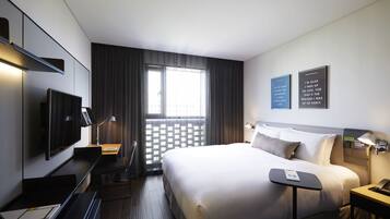 A modern hotel room with a large bed, a desk, a flat-screen TV, a desk lamp, and two motivational posters on the wall.