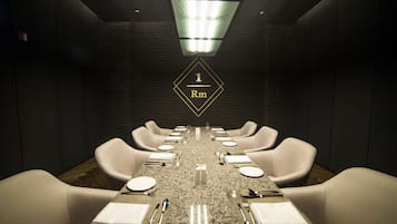 A conference room with a long table, white chairs, and a dark brick wall.