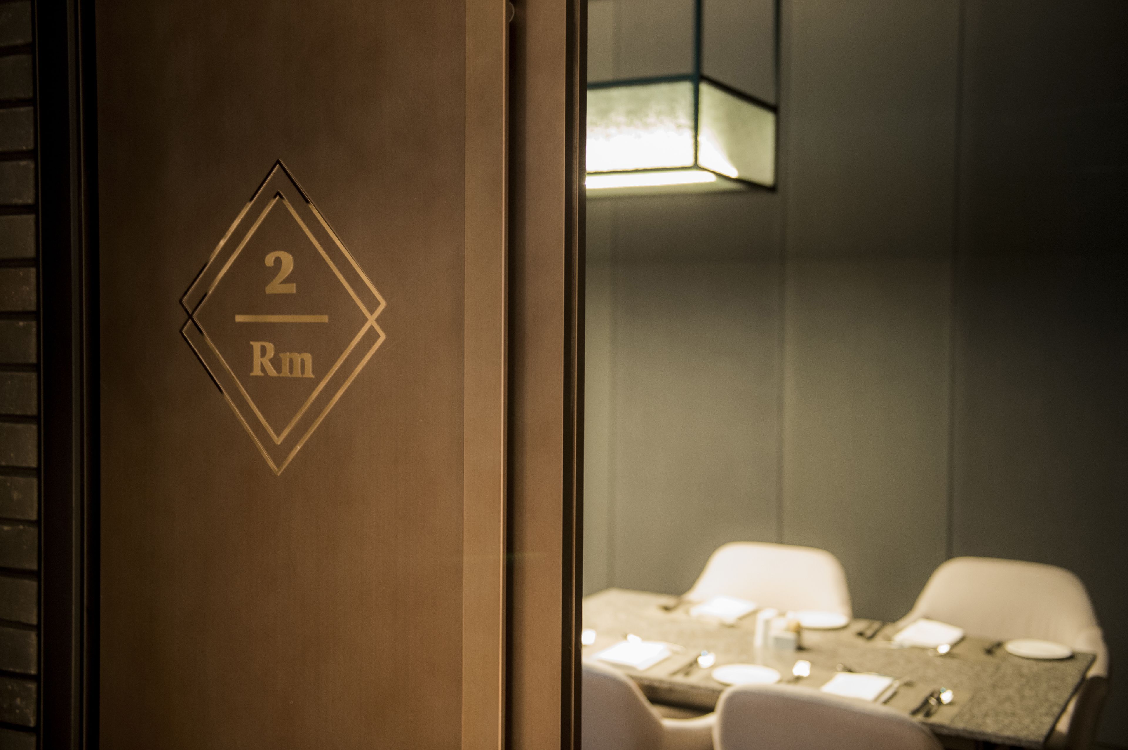 Habitación de hotel con una puerta de madera que indica "2 Rm" y un área de comedor con una mesa dispuesta para dos personas.