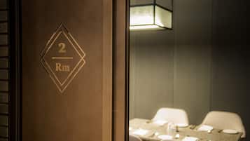 Habitación de hotel con una puerta de madera que indica "2 Rm" y un área de comedor con una mesa dispuesta para dos personas.