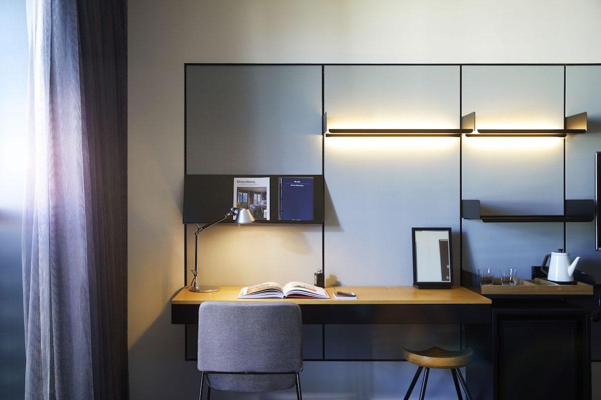 Une chambre d’hôtel moderne équipée d’un bureau, d’une chaise, d’une lampe et d’un miroir.