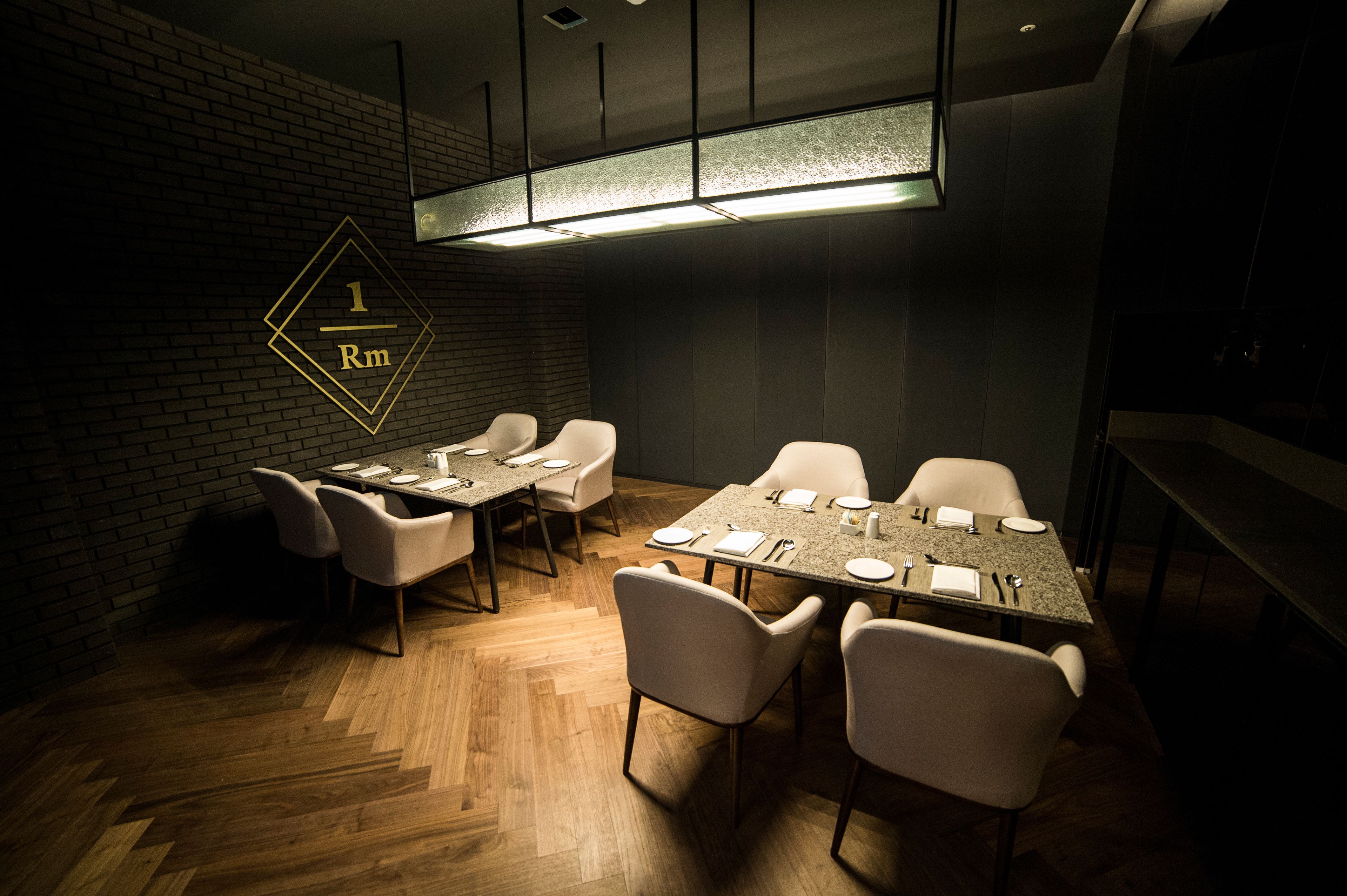 Un salón de conferencias con suelo de madera en patrón de espiga, sillas blancas, una larga mesa y una pared de ladrillo.