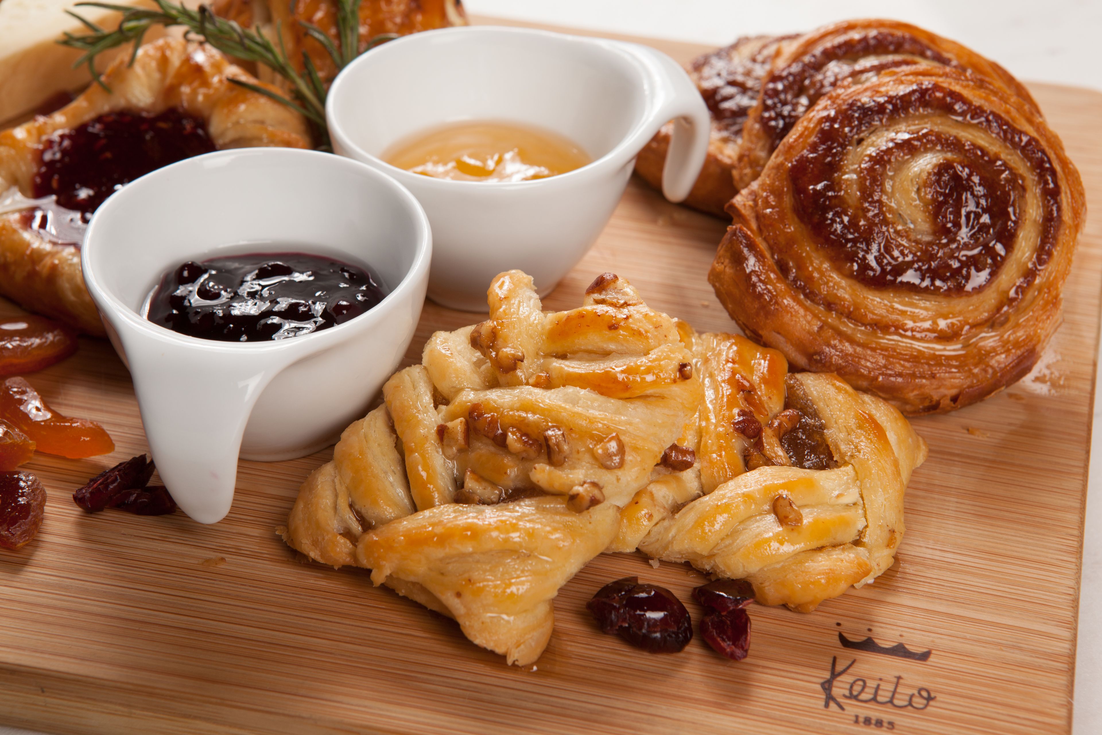 Une planche en bois sur laquelle sont disposés des pâtisseries, dont un pain aux cannelle, ainsi que deux petits bols de confiture.
