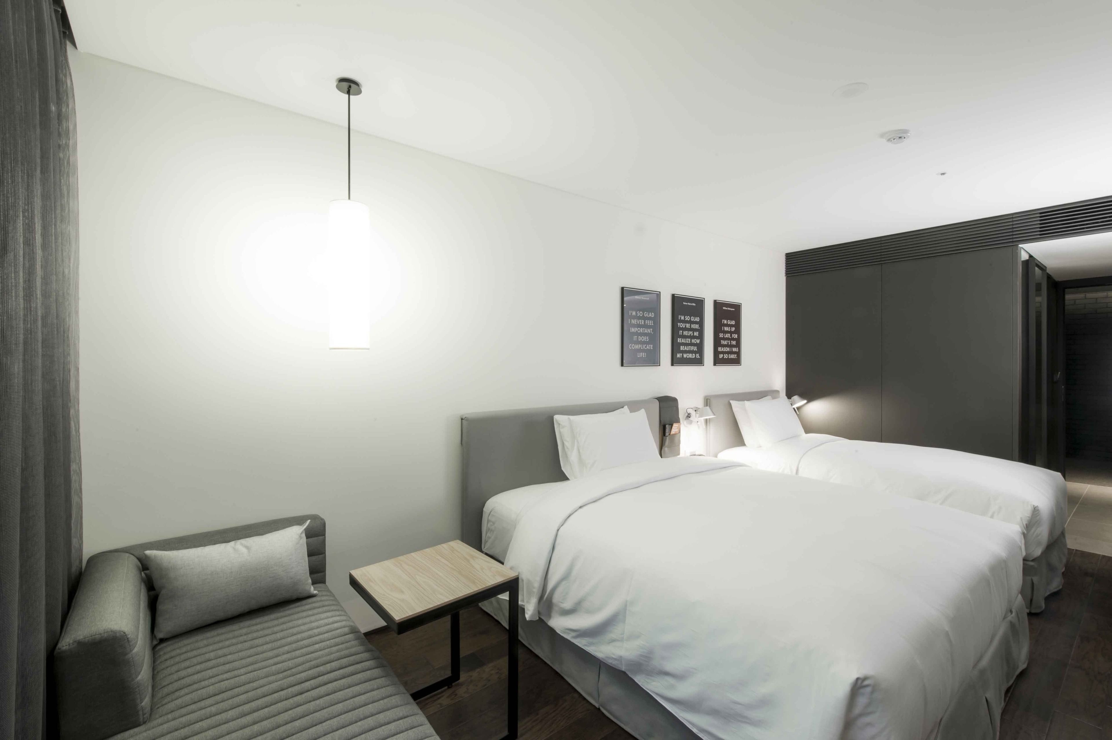 A modern hotel room with a large bed, a sofa, a small table, and a wall-mounted light fixture.