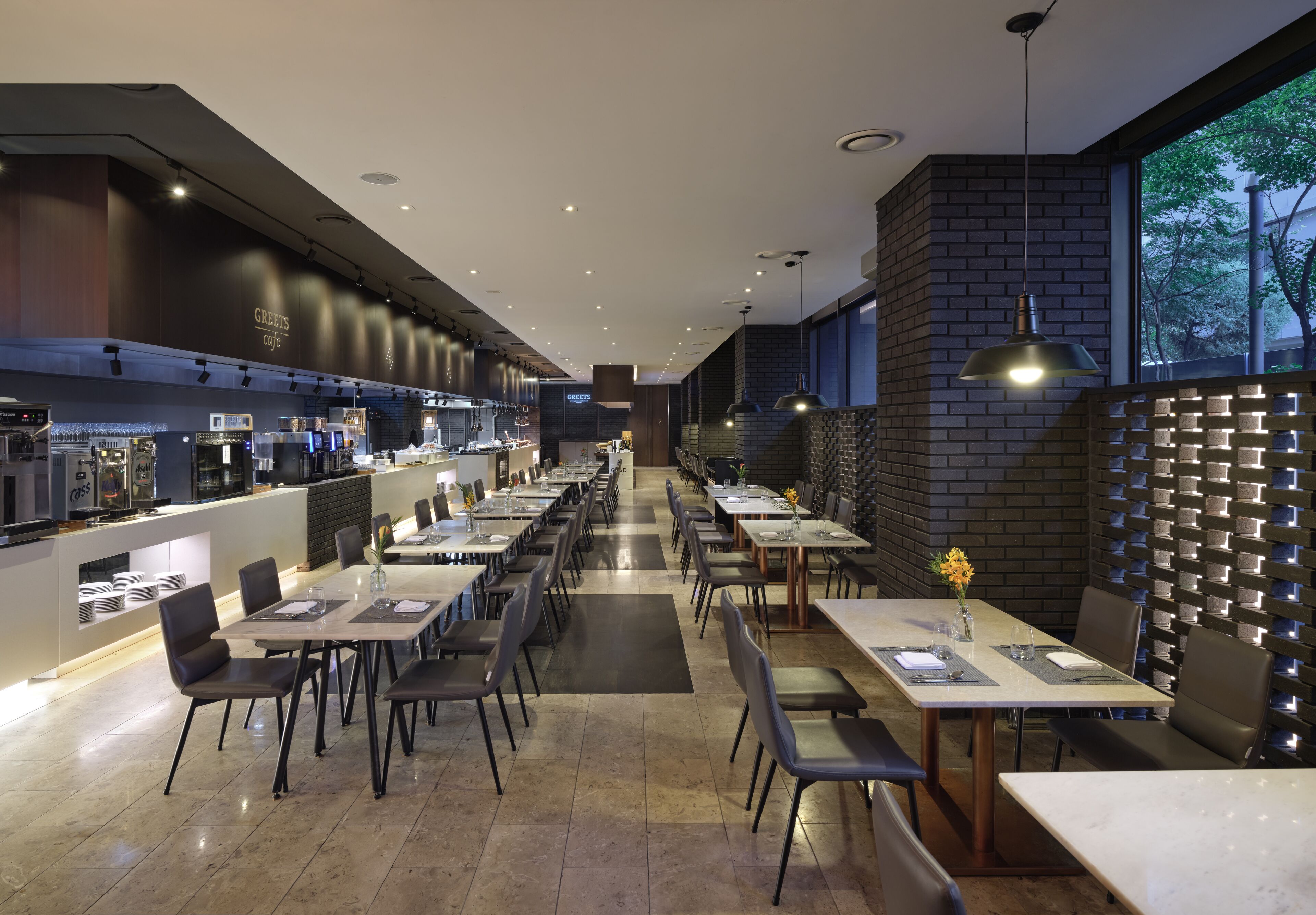A modern restaurant with a long counter, multiple tables, and a brick wall.
