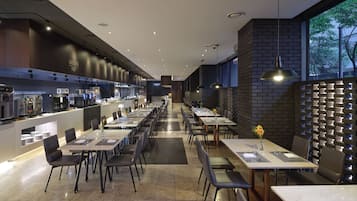 A modern restaurant with a long counter, multiple tables, and a brick wall.