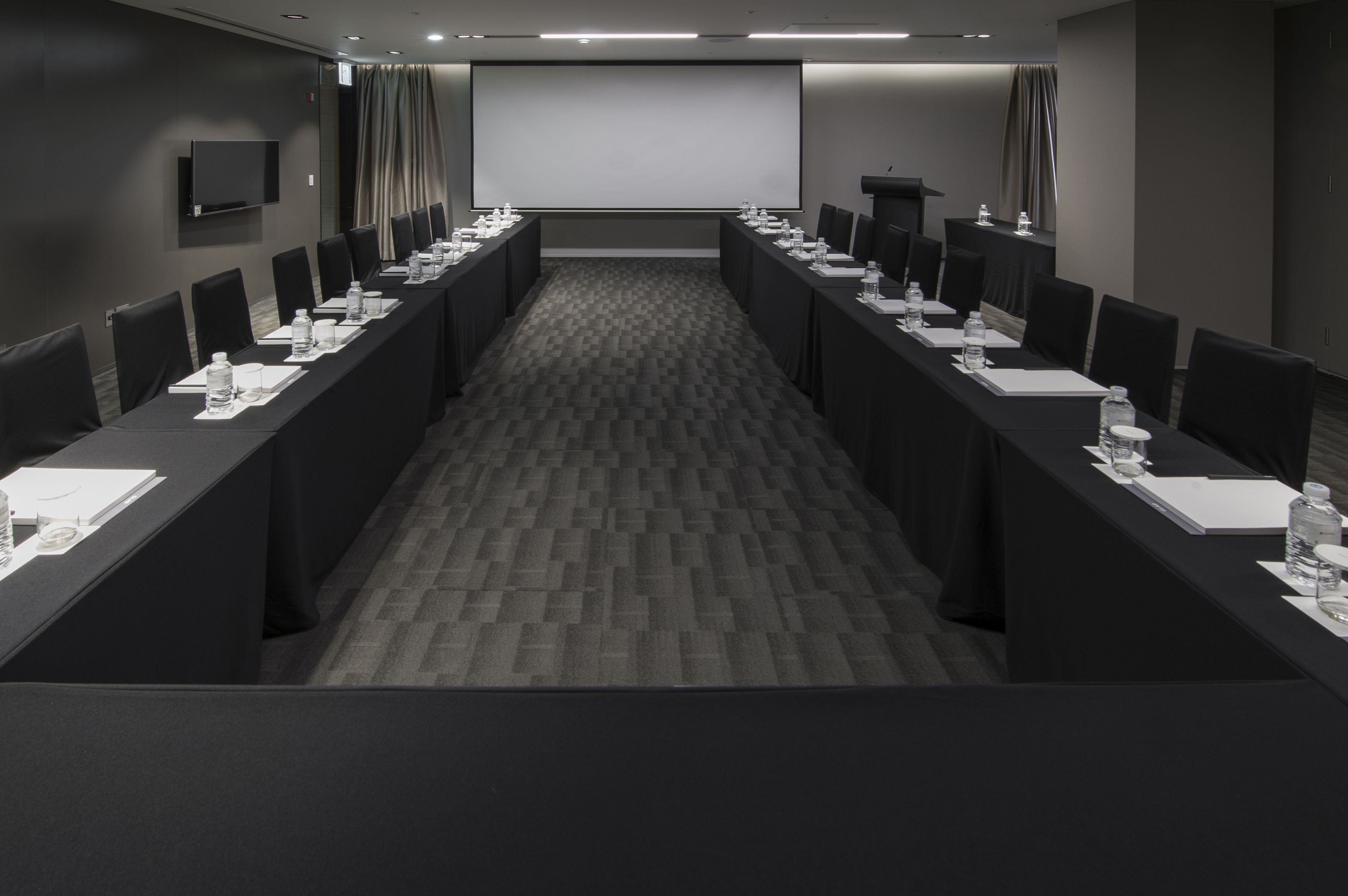 Uma sala de conferências com uma mesa comprida, cadeiras, um projetor e uma televisão de tela plana.