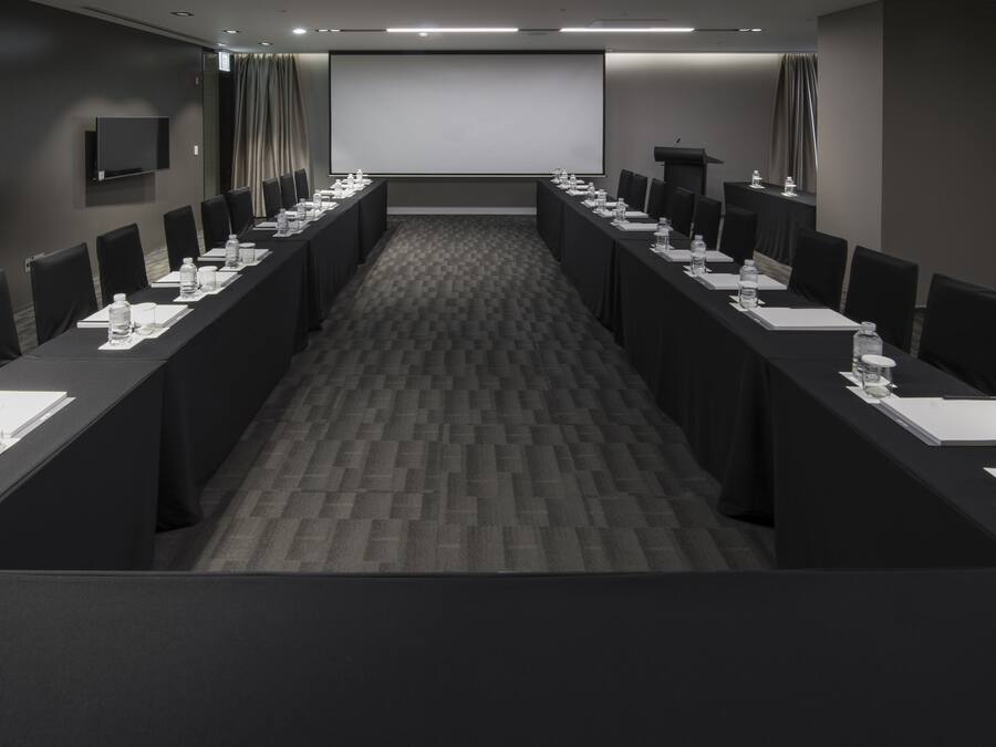 Uma sala de conferências com uma mesa comprida, cadeiras, um projetor e uma televisão de tela plana.