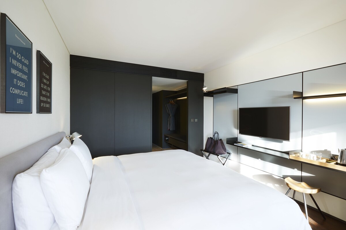 Une chambre d’hôtel moderne dotée d’un grand lit, d’une télévision à écran plat, d’un miroir et d’un dressing.