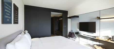 Habitación de hotel moderna con una cama grande, un televisor de pantalla plana, un espejo y un vestidor.