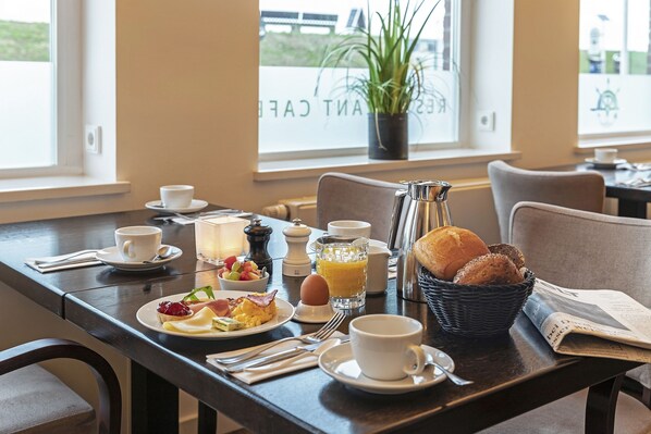 A breakfast table with a cup, a glass of orange juice, a basket of bread, a newspaper, and a plate of food.