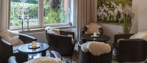 A cozy lounge area with leather sofas and ottomans, a round table with a candle, and a large painting of sheep on the wall.