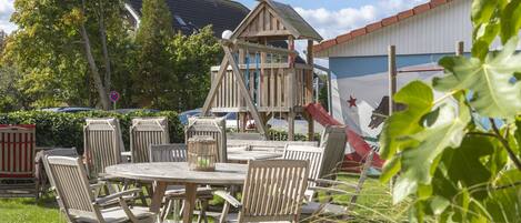 A wooden playhouse with a climbing wall, surrounded by outdoor furniture and a picnic table.