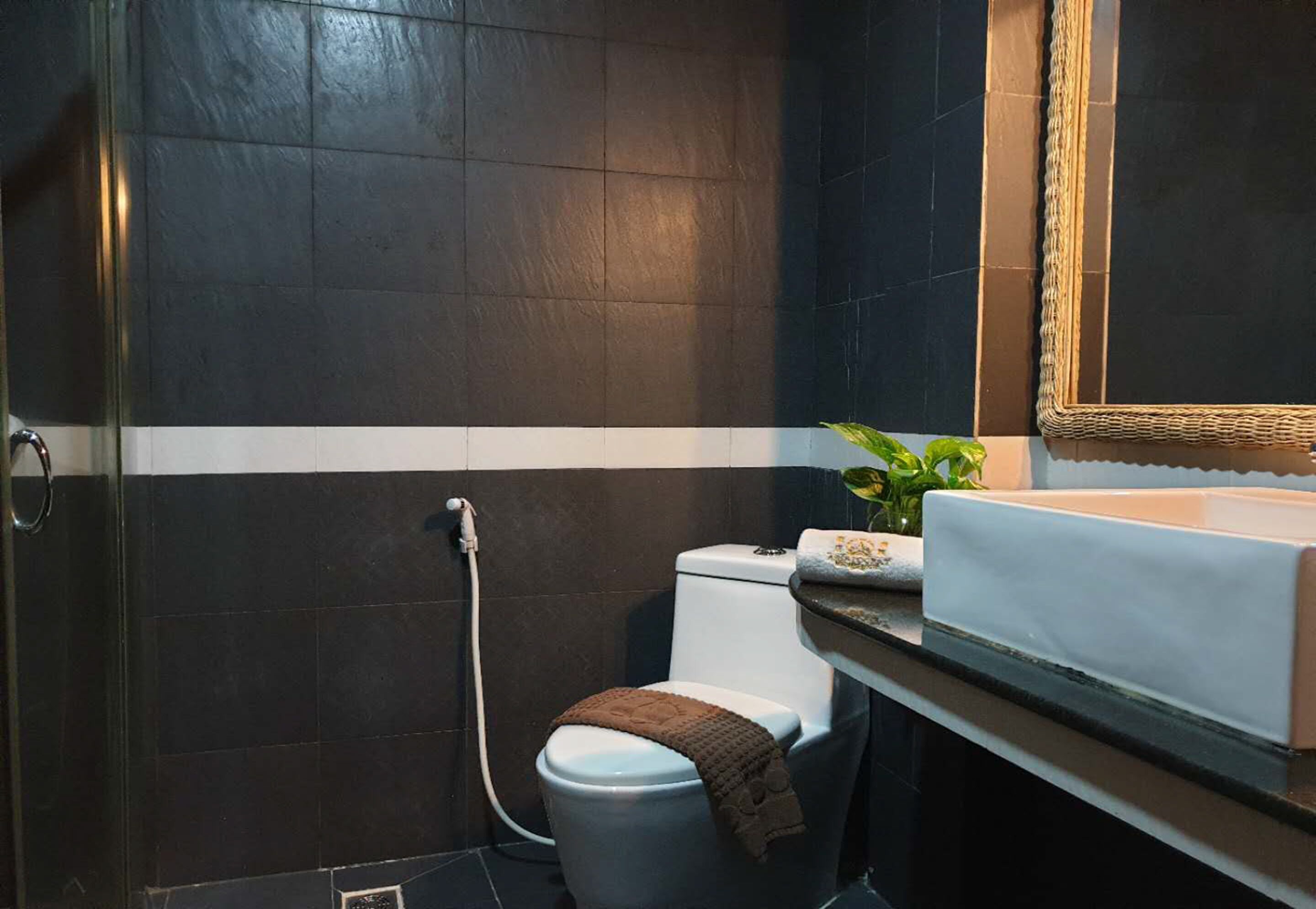 Ein modernes Badezimmer mit dunklen Fliesen, einer weißen Toilette, einer Dusche und einem Waschbecken mit Spiegel.