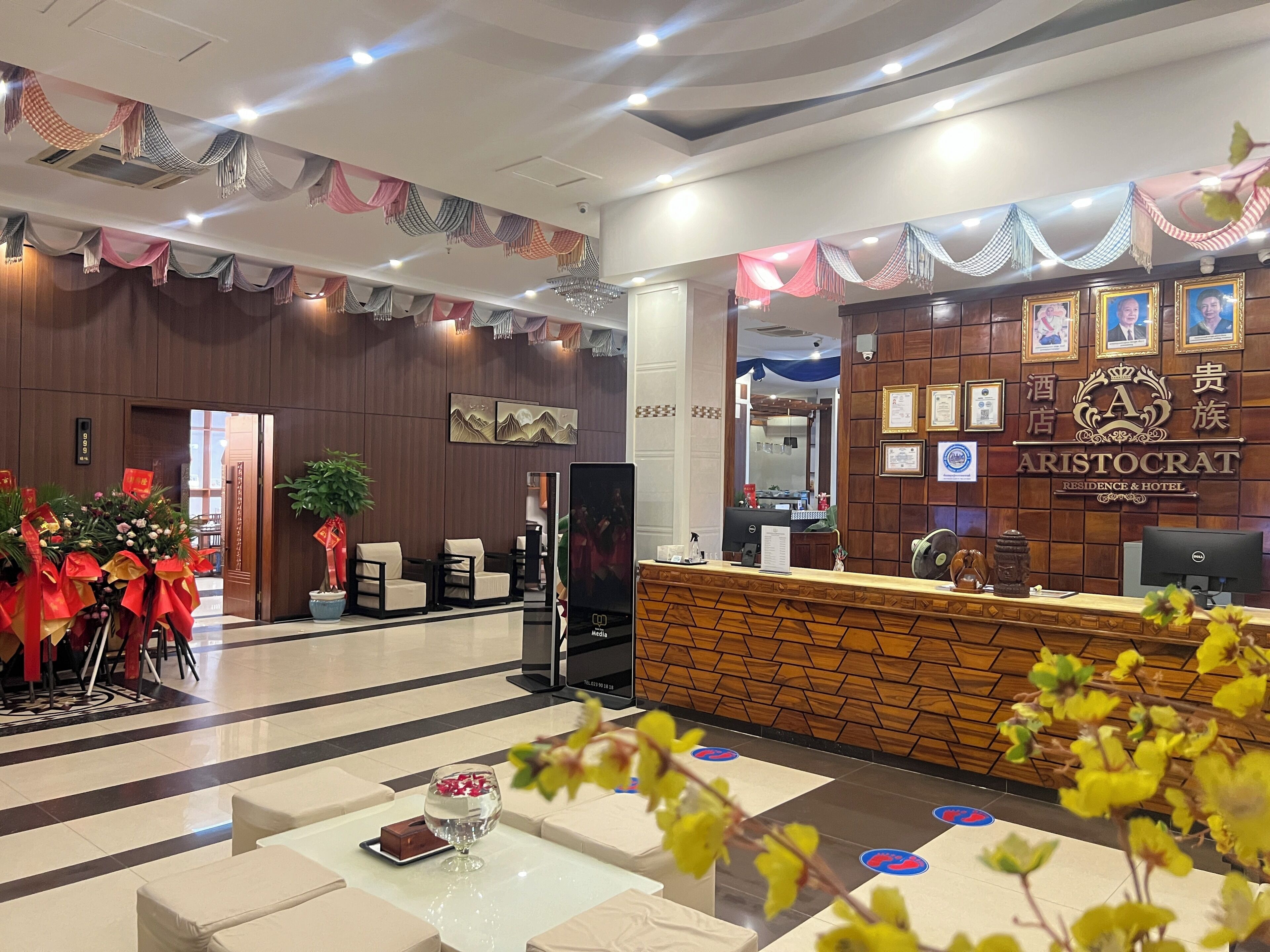 A hotel reception area with a wooden reception desk, framed pictures on the wall, and a large mirror.