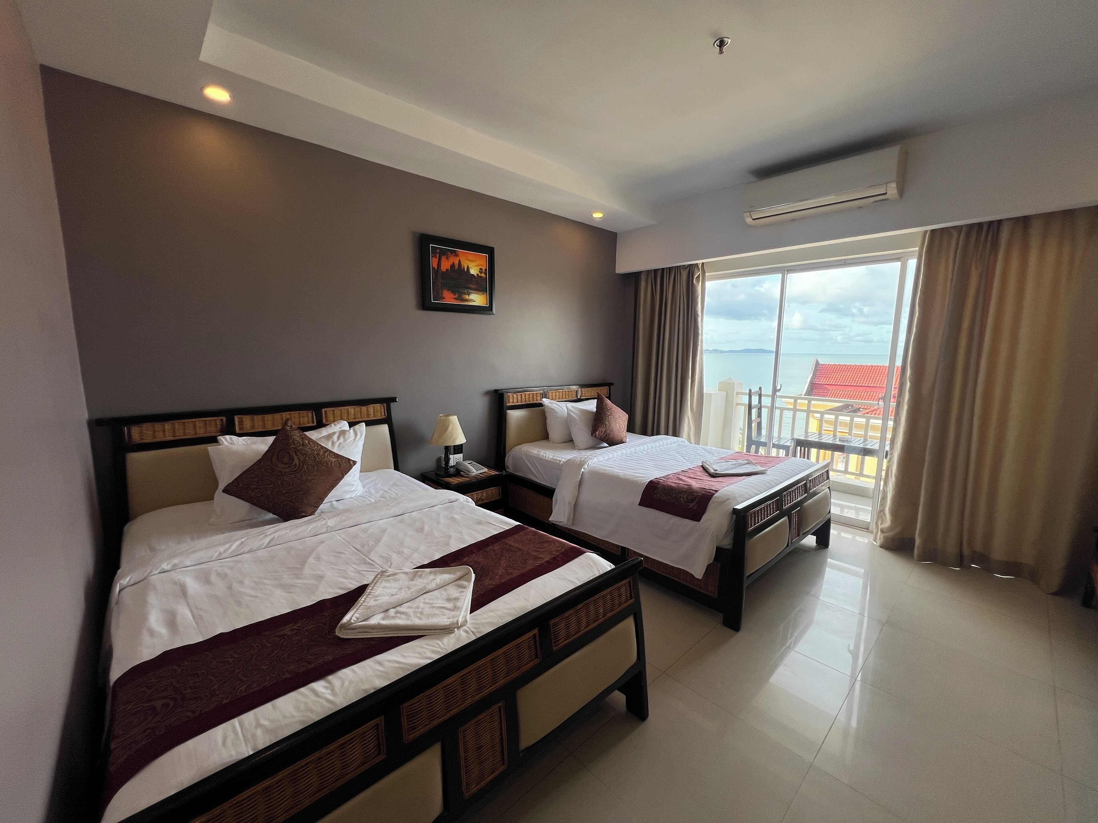 A hotel room with two beds, a large window with a view, and a ceiling fan.