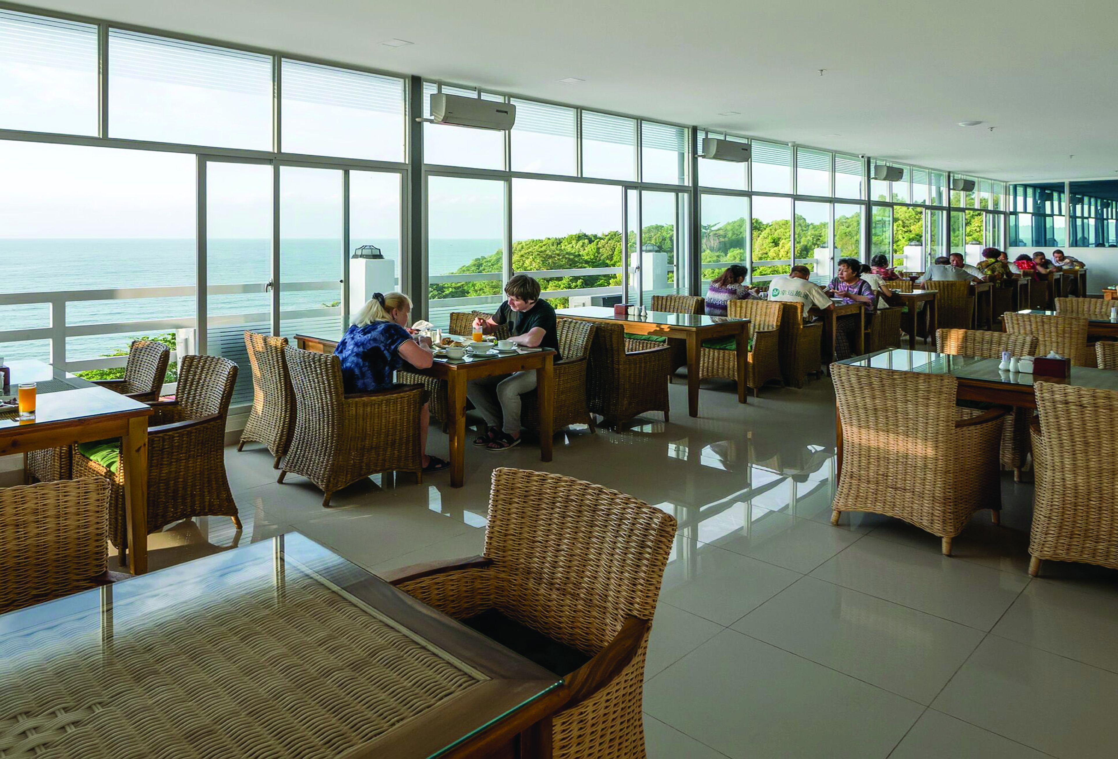 Una spaziosa sala da pranzo con mobili in vimini e ampie finestre che si affacciano sul mare.