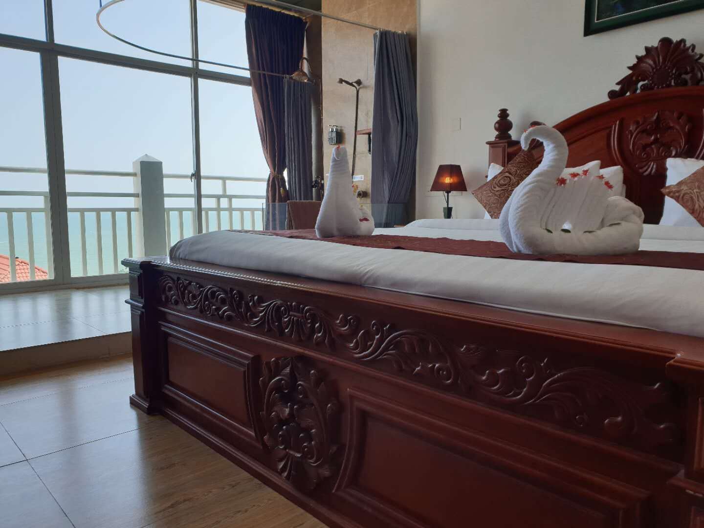 A spacious bedroom with a large bed, ornate wooden headboard, and a view of the sea through large windows.