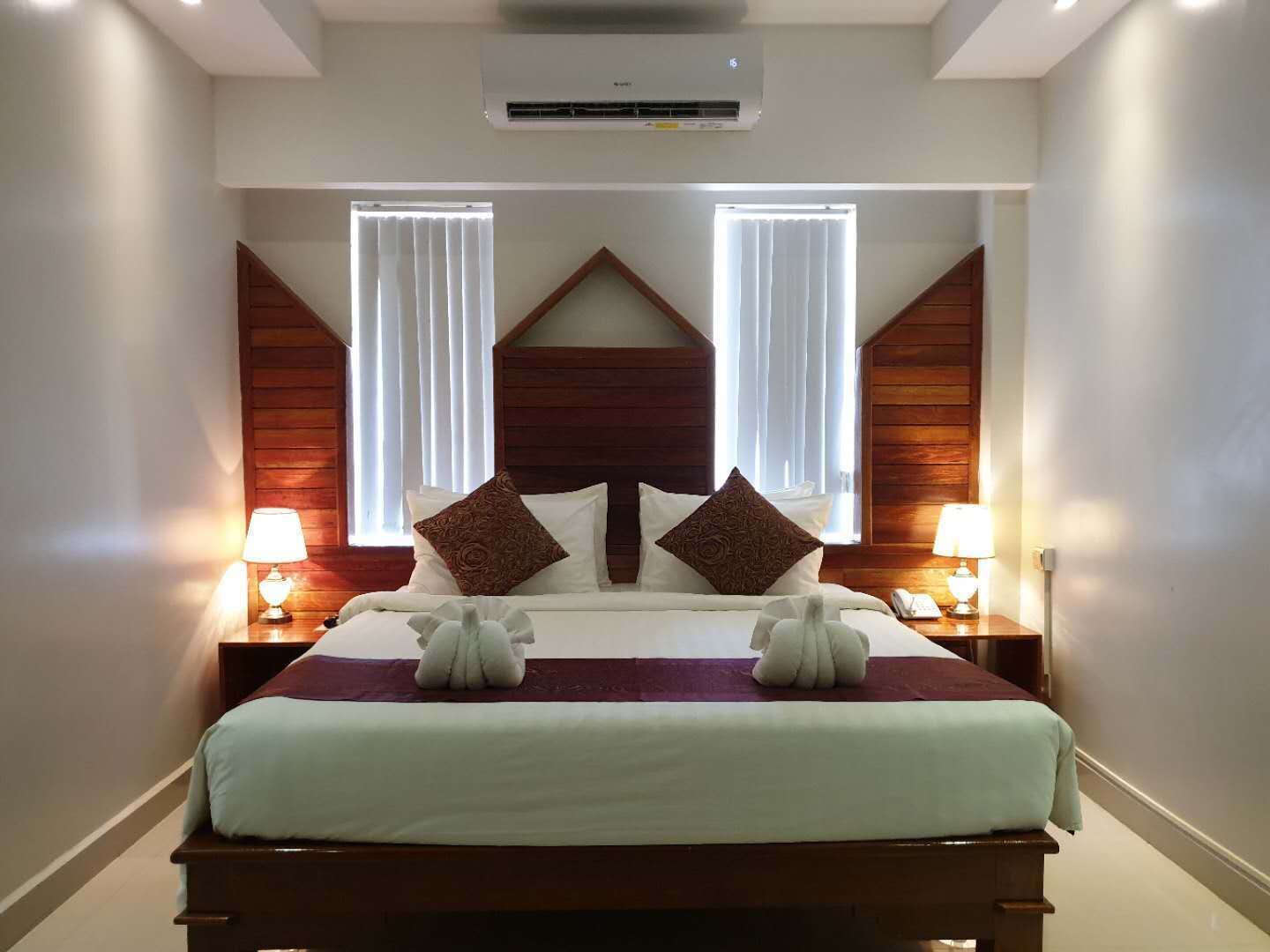 A hotel room with a large bed, two bedside lamps, and a modern air conditioning unit.