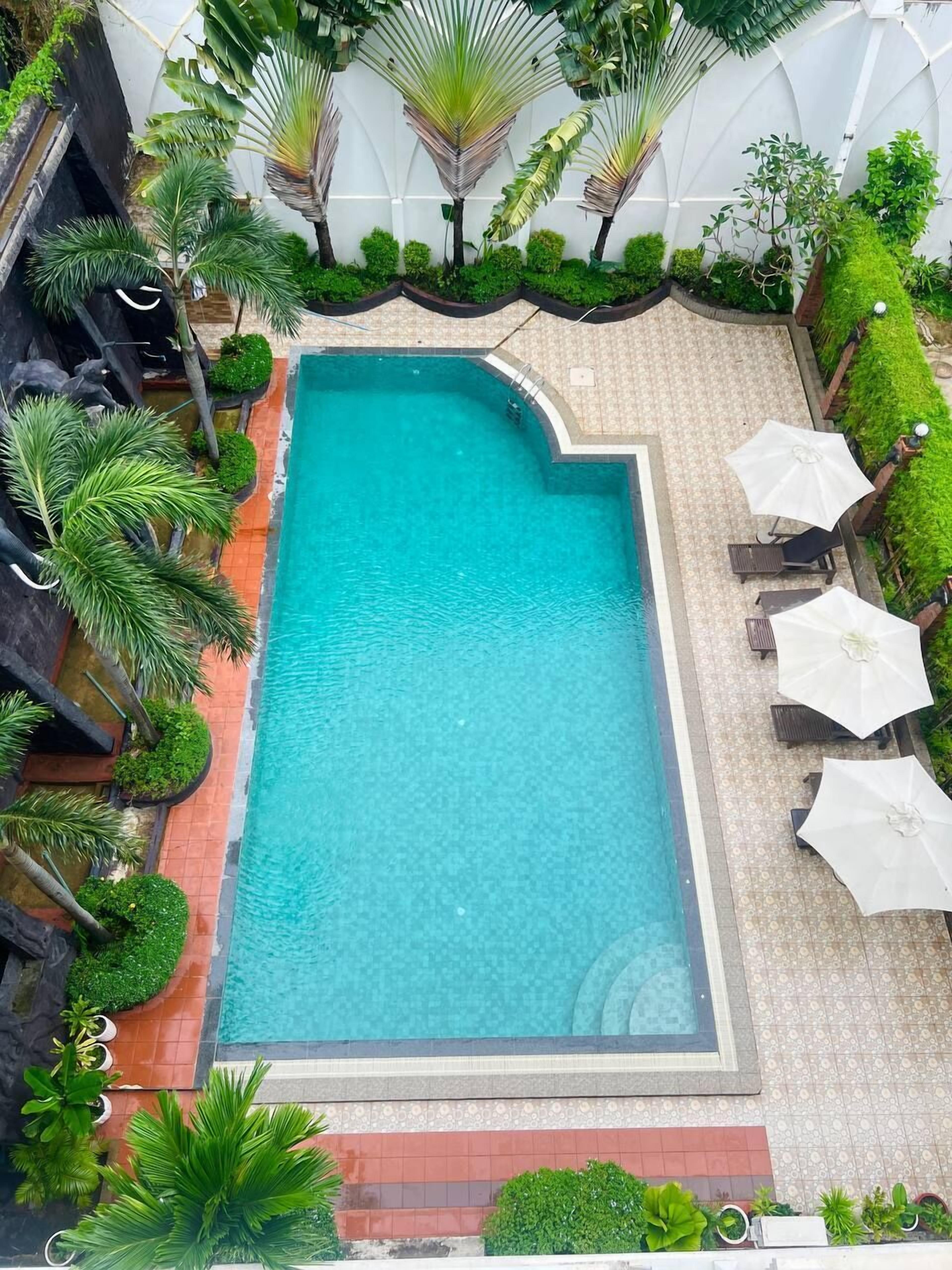 A rectangular pool with a tiled edge, surrounded by lush greenery and a tiled patio area with outdoor seating.