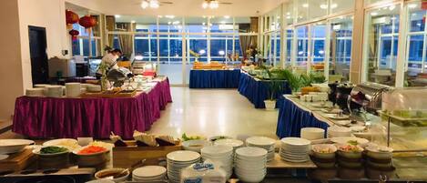 A buffet setup with multiple tables covered in tablecloths, food containers, and stacked plates.