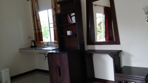 Quarto com armário de madeira escura, uma mesinha, uma estante com uma caixa e uma janela com cortinas.