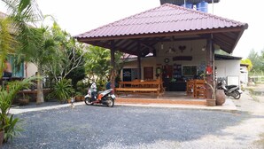 Uma área de estar coberta ao ar livre com bancos, uma motocicleta estacionada perto e um edifício com uma placa de sinalização ao fundo.