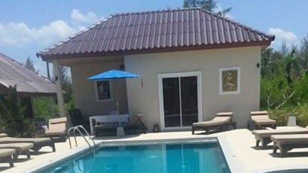 Piscina com piso de azulejos, espreguiçadeiras e um pequeno edifício com telhado ladrilhado.