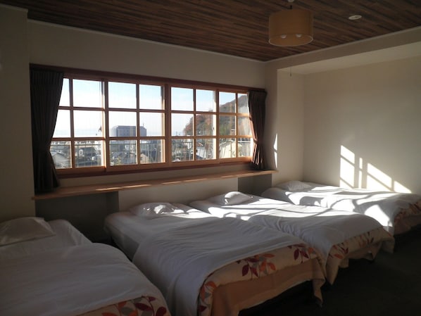 A room with three beds, a large window with curtains, and a wooden ceiling.
