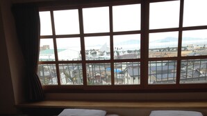 A hotel room with two beds, a large window with a view of the city, and a curtain on the left side. - Gamagori Orange Pension (Gamagori)