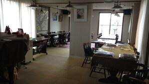 A dining area with tables and chairs, a large window, and ceiling fans. - Gamagori Orange Pension (Gamagori)