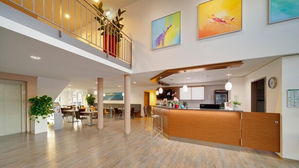 A spacious hotel lobby with a wooden reception desk, multiple seating areas, and a mezzanine level with a railing. - Euro Hotel Friedberg (Friedberg)