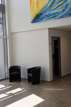 Un hall d’entrée moderne avec deux fauteuils noirs, une grande peinture abstraite et une porte ornée du logo Coca-Cola.