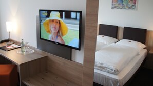 A hotel room with a flat-screen TV mounted on the wall, a desk with a lamp, a bottle, and a glass, and a bed with white bedding. - Euro Hotel Friedberg (Friedberg)