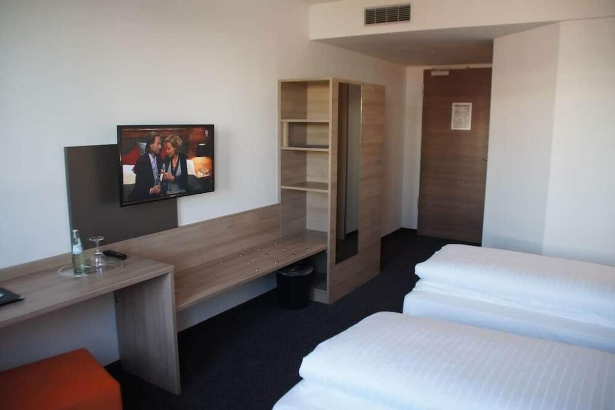 Una habitación de hotel con cama, escritorio, televisor y armario.