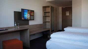 Una habitación de hotel con una cama, un escritorio con una computadora, un televisor y un taburete pequeño color naranja.