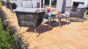 An outdoor seating area with wicker furniture and a table, a white umbrella, and a building with large windows and a red facade in the background. - Euro Hotel Friedberg (Friedberg)