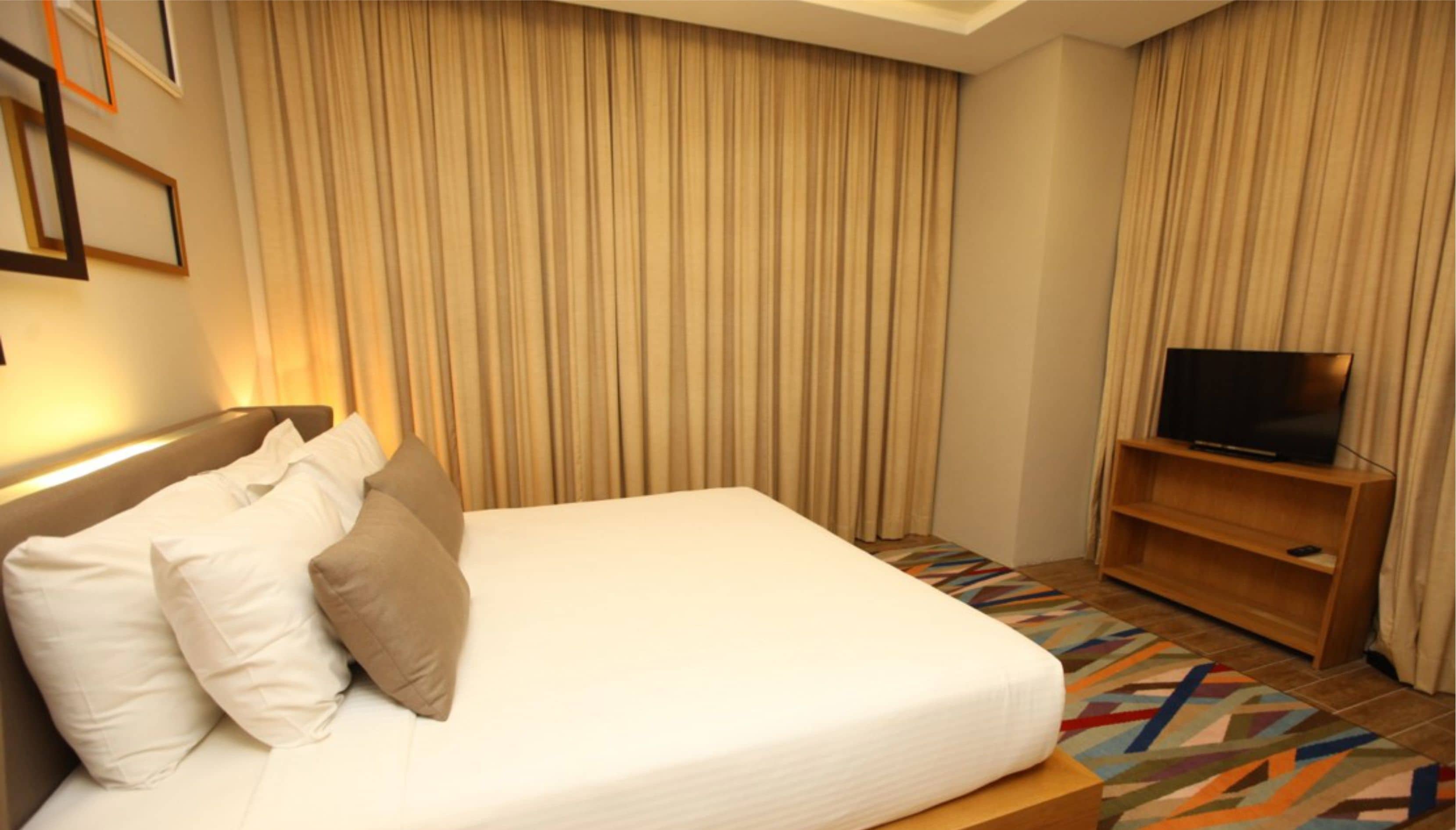 Ein Hotelzimmer mit einem Bett, Kissen, einem Fernseher auf einem Holzständer und einem gemusterten Teppich.