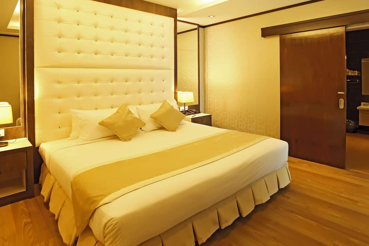 Una cama grande con cabecera capitonada, una mesita de noche con lámpara y suelo de madera.