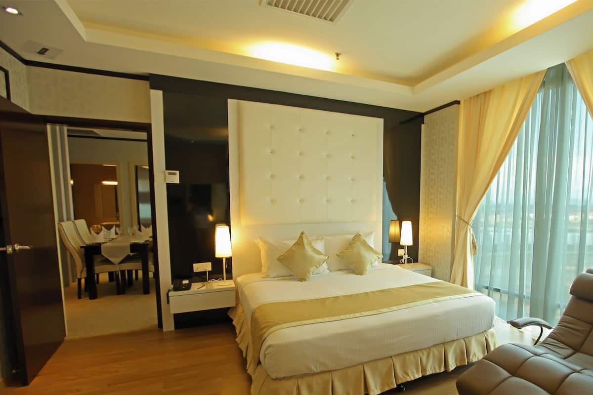 Una habitación de hotel con una cama grande, lámparas de noche, una silla, un escritorio con silla y un ventanal con cortinas.